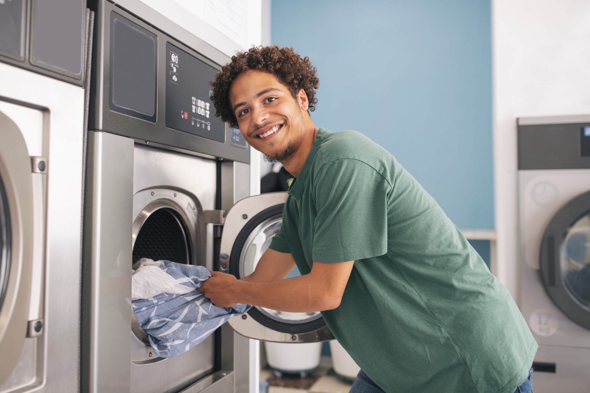 Latin Young Guy Loading Washing Machine Posing At Laundrette Room