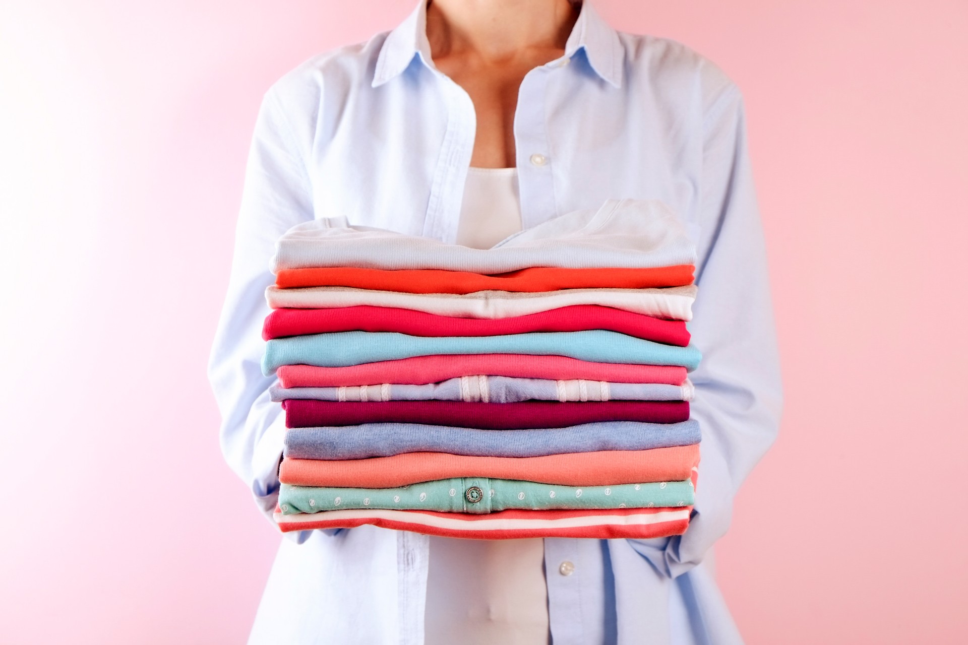 Female holding a pile of folded clothes, unisex for both man & woman, different color & material. Trip preparation concept.